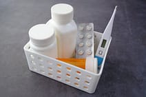 gallery-4 Healthcare basket with medication bottles, pills, and thermometer on a dark surface.