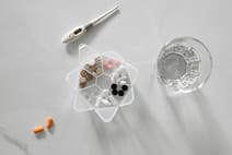 gallery-5 Overhead view of assorted medications with glass of water and digital thermometer on white background.