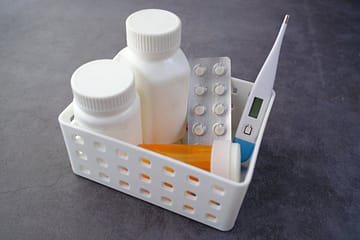 ours-journey Healthcare basket with medication bottles, pills, and thermometer on a dark surface.