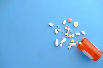 pexels photo 9155926 An assortment of colorful pills scattered from a prescription bottle on a blue background.